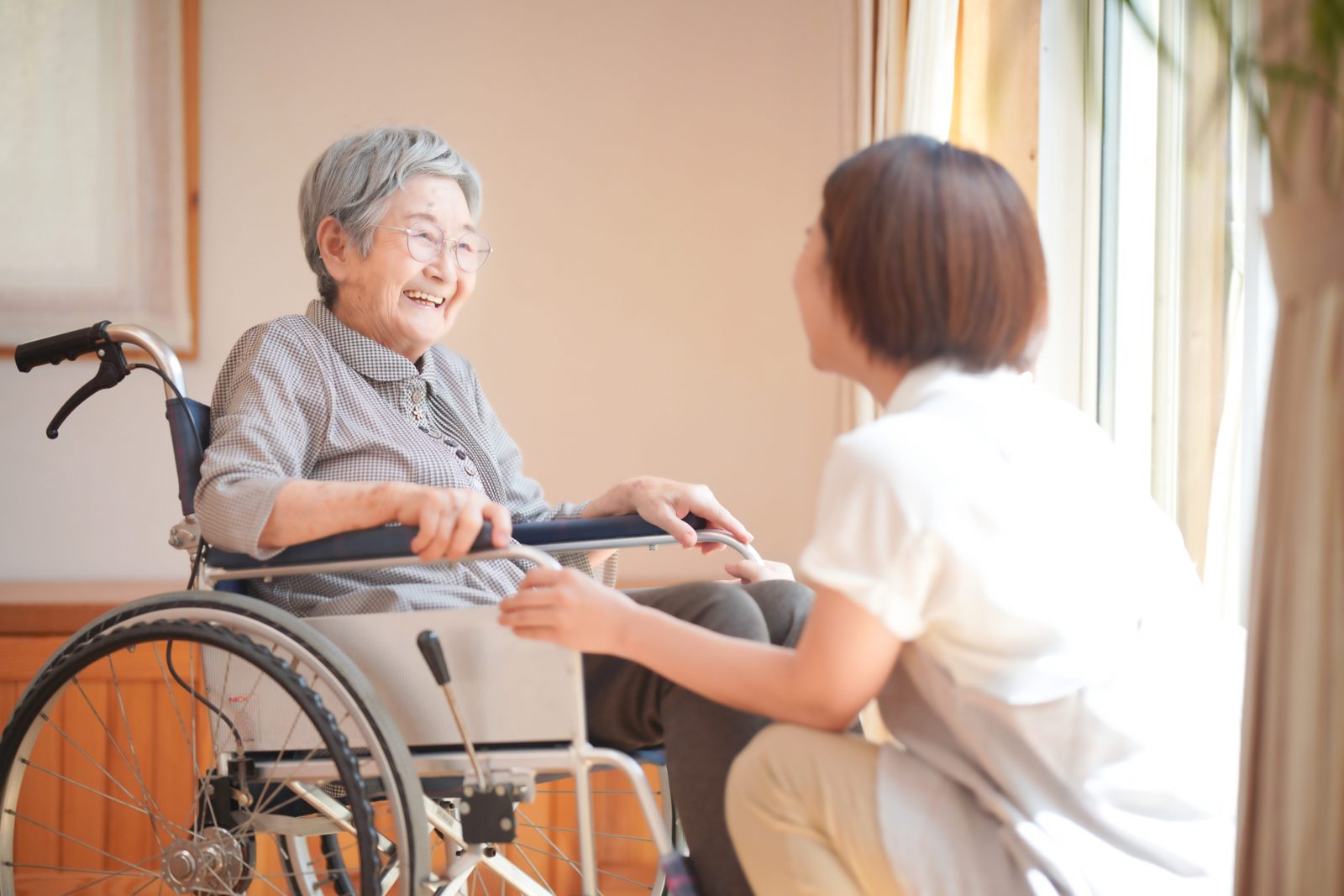 車椅子に座る高齢の女性と向き合い、話を聞くスタッフ