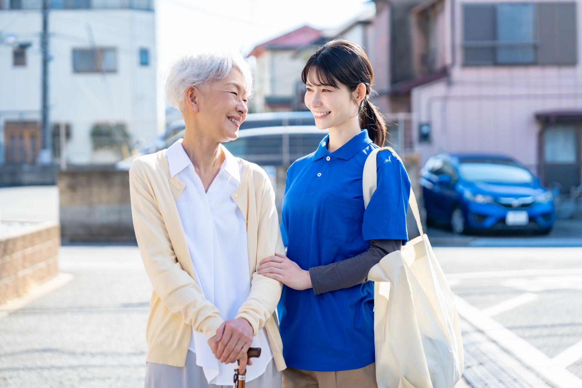 杖をついた高齢の女性に寄り添い、腕を支えて歩くスタッフ